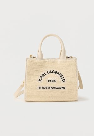Beige geweven handtas met korte handvatten, verstelbare riem en de tekst "Karl Lagerfeld Paris 21 Rue St-Guillaume" in het zwart gedrukt op de voorkant.