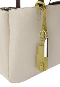 Beżowa skórzana torba na ramię o gładkiej fakturze, z jasną zieloną metką i srebrnymi akcentami. Prosty geometryczny design z podwójnymi uchwytami.