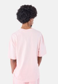 Camiseta de algodón rosa claro con un ajuste relajado, mangas cortas y cuello redondo. La parte posterior muestra una textura suave y detalles de diseño mínimos.