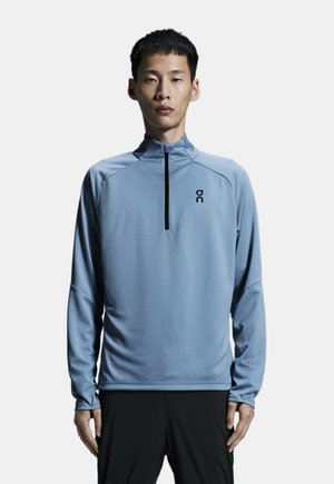 Hellblaues, langärmliges Sportoberteil mit Halbreißverschlusskragen, aus glattem Stoff, mit Raglanärmeln und kleinem Logo auf der Brust.