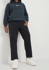 Granatowa bluza z kapturem z przednią kieszenią i białym logo, zestawiona z czarnymi jeansami o prostych nogawkach i białymi trampkami z fakturalnymi detalami.