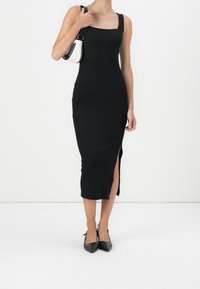 Czarna dopasowana sukienka midi z kwadratowym dekoltem, bocznym rozcięciem i grubymi ramiączkami. Stylizowana z czarnymi czółenkami na szpilce i małą torebką w dwóch kolorach.