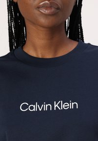 Marineblå bomulls T-skjorte med rund hals som har hvit "Calvin Klein" logo trykket foran. Jevn tekstur, avslappet design.