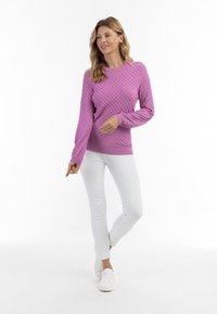 Fuchsia-farbener, strukturierter Pullover mit rundem Halsausschnitt, langen Ärmeln und gerippten Bündchen, kombiniert mit weißen, enganliegenden Hosen und weißen Sneakers.