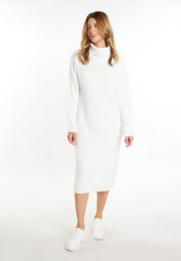 Abito midi lavorato a maglia bianco con collo alto, maniche lunghe e vestibilità comoda, abbinato a sneakers bianche. Texture liscia, design minimale.