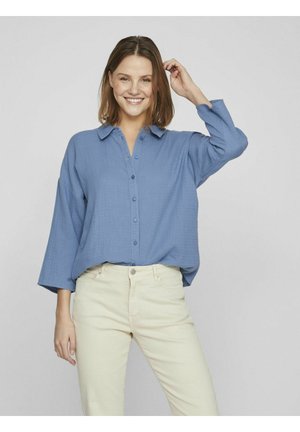 Light blue button-up shirt with a relaxed fit, long sleeves, and a textured fabric, paired with beige pants.