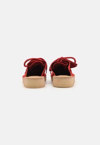 Red suede slip-on shoes with a textured surface, rounded toes, and a cork sole, featuring a tied ribbon detail at the back.