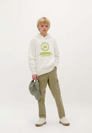 Witte hoodie met groene grafische print, khaki cargo pants met zijzakken, grijze baseballcap en witte sneakers met beige zolen.