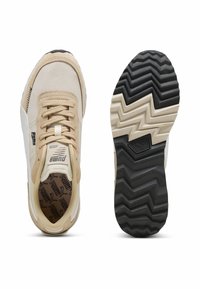 Zapatillas deportivas beige y blancas con materiales de malla y ante. Presentan una suela de goma negra texturizada con un patrón de zigzag y marca.