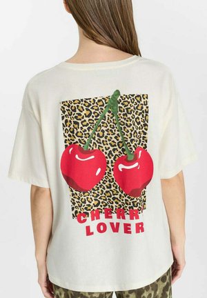 Persona che indossa una t-shirt bianca con una grande grafica di ciliegia e un quadrato in stampa leopardata, testo "CHERRY LOVER" in rosso sulla schiena.