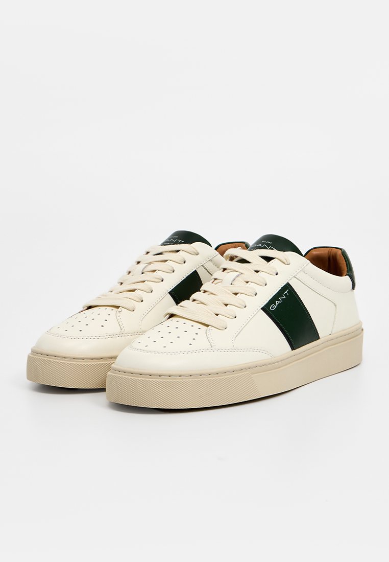 Zapatillas de cuero blancas con detalles en verde, puntera redonda, perforaciones decorativas, suela beige y cordones planos. Logo de la marca en el lateral.