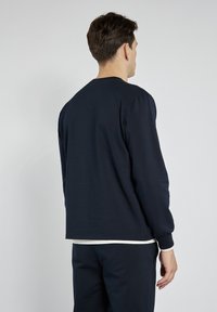 Granatowa longsleeve wykonana z bawełny, z okrągłym dekoltem i lekko bufiastymi ramionami, w luźnym kroju i z prążkowanymi mankietami.