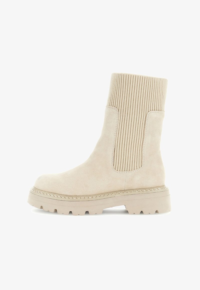 Beige ruskindsankelstøvle med ribbet strik elastisk sidepanel og tyk sål på en hvid baggrund.