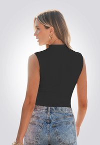 Top nero senza maniche con scollatura alta, abbinato a jeans in denim chiaro aderenti con tasche posteriori e una leggera scoloritura.