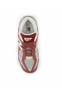 Zapatilla deportiva en color marrón y gris, hecha de materiales de malla y gamuza, que presenta una suela acolchada, acentos triangulares y un diseño con cordones.