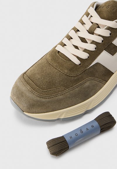 Αθλητικό παπούτσι από πράσινο σουέντ χρώμα ελιάς με κρέμ κορδόνια και λευκές λογότυπες λεπτομέρειες. Περιλαμβάνει ένα ζευγάρι καφέ κορδόνια σε μπλε ετικέτα.