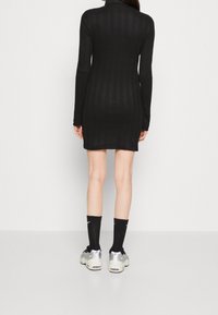 Robe noire côtelée à manches longues avec une silhouette ajustée, dotée d'un col montant. Associée à des chaussettes noires et des baskets épaisses.