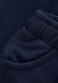 Donkerblauwe stof die een close-up van een zak toont met een zachte textuur en ribbelrand, met een elastische band aan de bovenkant voor een verstelbare pasvorm.