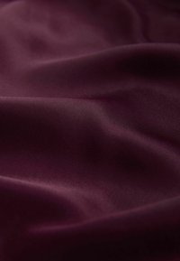 Tissu bordeaux à texture lisse, affichant de doux plis ondulés et un éclat subtil, mettant en valeur son design léger et fluide.