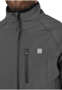 Grau weiche Softshelljacke mit hohem Kragen, Frontreißverschluss und aufgesetzter Brusttasche mit Reißverschluss. Merkmale ein kleines gestreiftes Logo auf der Brust. Glatte Textur.