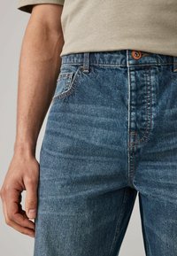 Jeans din denim de culoare bleo deschis, cu un finisaj texturat. Prezintă o închidere cu bătaie, cinci buzunare și cusături contrastante de-a lungul cusăturilor.