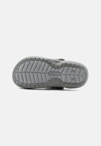 Semelle de chaussure en caoutchouc gris avec un motif de semelle texturé, présentant un logo circulaire et des rainures pour une meilleure adhérence. Fini lisse dans l'ensemble.