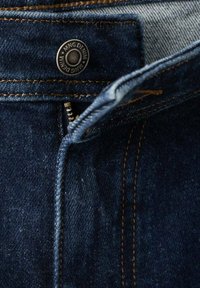 Dunkelblaue Jeans aus Denim mit teilweise geöffnetem Reißverschluss und einem Metallknopf am Bund, der mit "MNG DENIM" graviert ist.