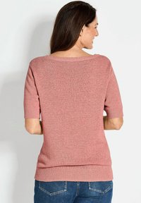 Kurzärmliger, rosa gestrickter Pullover mit lockerer Passform, geripptem Ausschnitt und Saum. Kombiniert mit Jeans aus Denim, die eine weiche Textur zeigen.