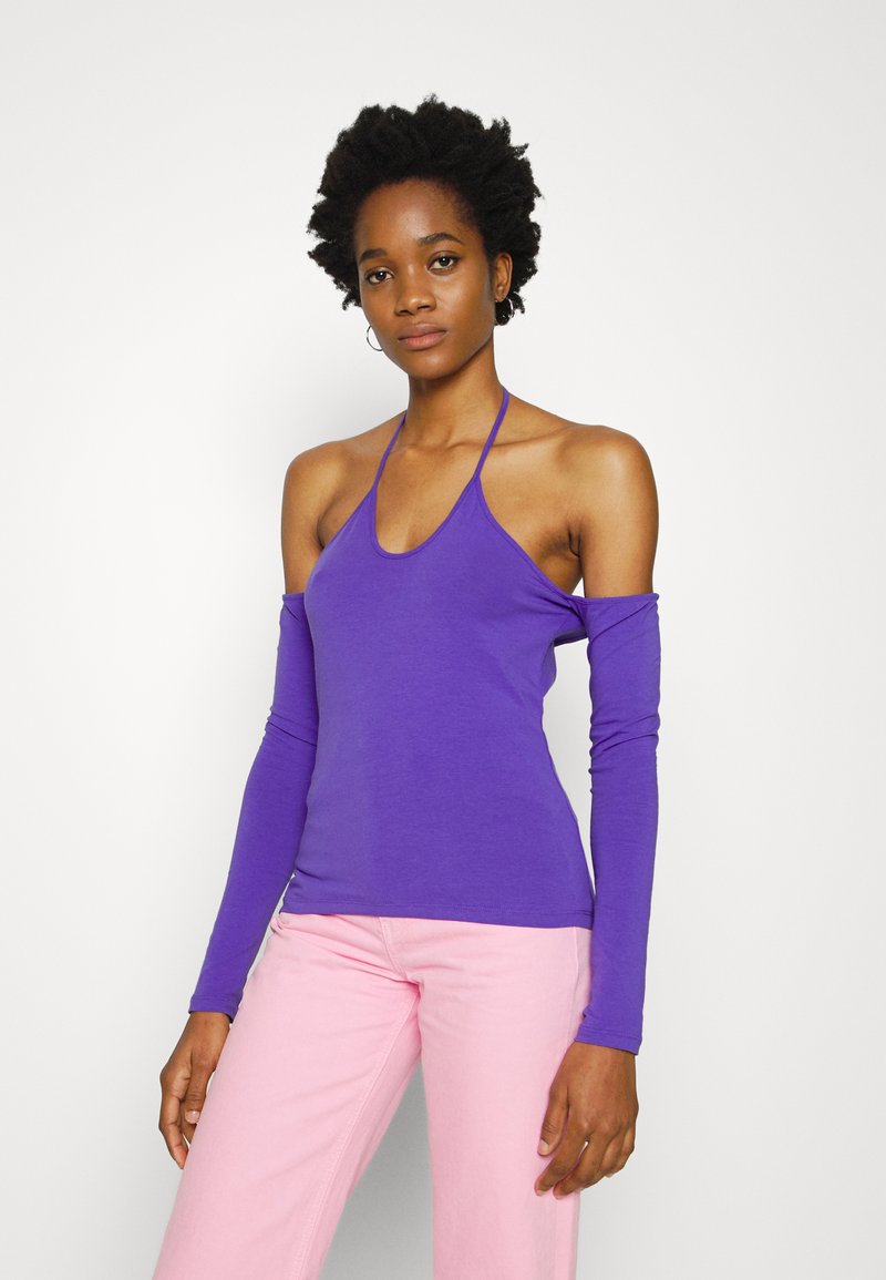 Top halter roxo com mangas longas, feito de tecido suave. Apresenta um decote profundo e um design ajustado. Combinado com calças rosa claras.