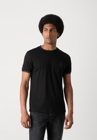 Zwarte kortekoot T-shirt met een ronde halslijn, voorzien van een subtiele berenlogo op de linkerborst en contrasterende mouwaccenten.