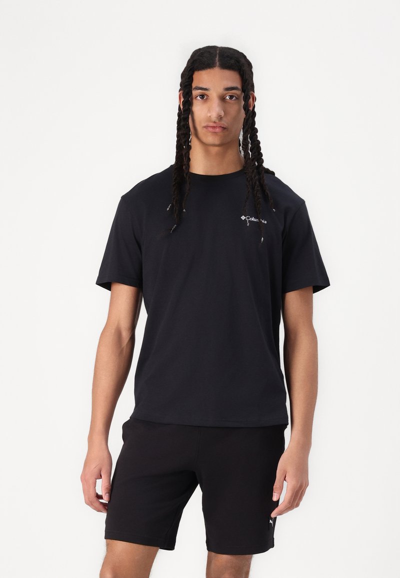 T-shirt en coton noir à manches courtes et col rond, avec un logo subtil sur la poitrine. Porté avec un short noir.