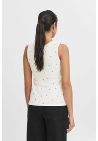 Haut sans manches en côte de couleur blanc cassé, agrémenté d'un motif de cœurs rouges éparpillés et d'une coupe ajustée, associé à un pantalon sombre.