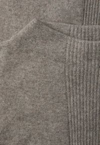 Harmaa neulottu kangas, jossa on sileä pinta ja kyljessä resorimainen osio. Hienovaraiset värivaihtelut luovat syvyyttä materiaaliin.