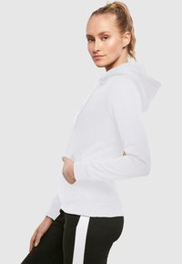 Hvit hettegenser med snorhette og frontlomme. Har lange ermer med ribbekant, glatt tekstur og uformell design.