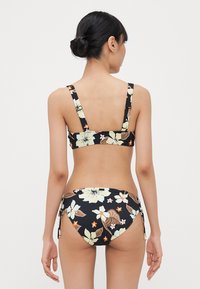 Czarny bikini w kwiaty z jasnymi żółtymi i pomarańczowymi akcentami, z regulowanymi ramiączkami i detalami w postaci zawiązań po bokach dolnej części.