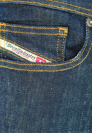 Jeans in denim blu scuro con cuciture arancioni, una piccola tasca frontale e un'etichetta visibile con la scritta "Diesel Industry Denim Division".