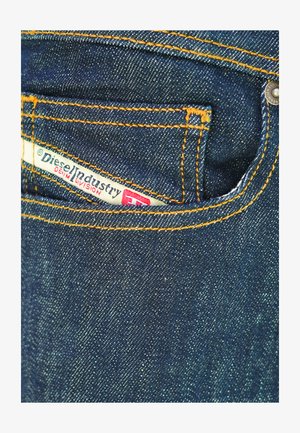 Jeans in denim blu scuro con cuciture arancioni, una piccola tasca frontale e un'etichetta visibile con la scritta "Diesel Industry Denim Division".