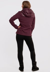 Mørkerød softshell-jakke med quiltet hætte, sømløs skulderdetalje og tætsiddende design, parret med sorte leggings og støvler.