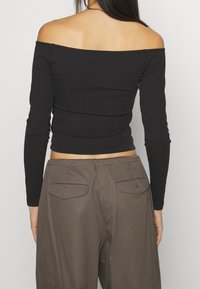 Schwarzes, geripptes Off-Shoulder-Oberteil mit langen Ärmeln, kombiniert mit khakifarbenen Cargo-Hosen mit Rückentaschen und einem entspannten Schnitt.