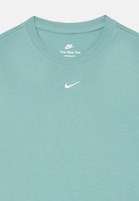 T-shirt en coton bleu clair avec un col rond et des manches courtes. Présente un petit logo Nike blanc centré près du col.