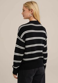 Svartvitrandig tröja med ribbad struktur, med rundad halsringning och långa ärmar. Manschetterna och fållen är fitted.