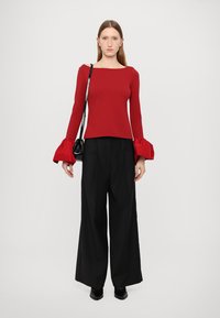Red fitted top with long, flared sleeves and a square neckline paired with high-waisted, wide-leg black trousers. Black handbag accessory.