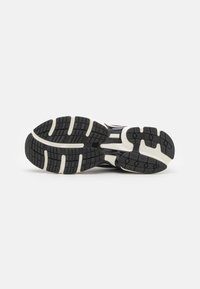 Suela de zapato atlético negro con una superficie de goma texturizada, que presenta acentos blancos y patrones de banda distintivos para mayor tracción.