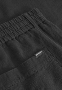 Black cotton pants featuring an elastic waistband, side pocket, and a small labeled tag. The fabric texture appears soft and smooth.