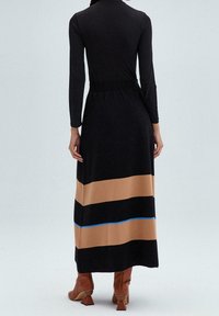 Vestido largo negro con mangas largas, cintura elástica y sección inferior en bloques de color marrón con detalle azul. Tela lisa y corte recto.