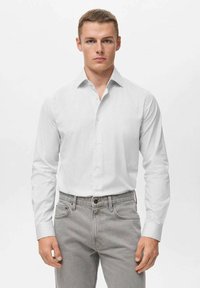 Witte, lang- en kortmouwige blouse met een subtiel gestreept patroon, gedragen met lichtgrijze jeans. Heeft een klassieke kraag en knoopmanchetten.