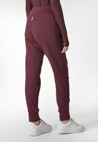 Bordeaux joggers met een gladde textuur, taps toelopende benen, elastische tailleband en boorden bij de enkels, gedragen met witte sneakers.