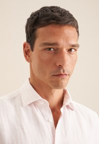 Camicia button-up a righe di un rosa chiaro, con un tessuto morbido e texture, colletto classico, caratterizzata da bottoni bianchi e un taglio rilassato.