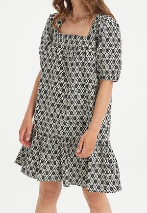 Robe à motifs noir et blanc avec encolure carrée, manches bouffantes et ourlet à volants. Le tissu semble léger et texturé.