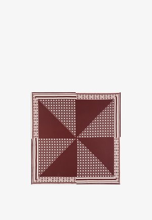 Femme portant un grand foulard en soie marron et beige à motifs, drapé sur une épaule, associé à un haut crème à manches longues et un pantalon foncé.